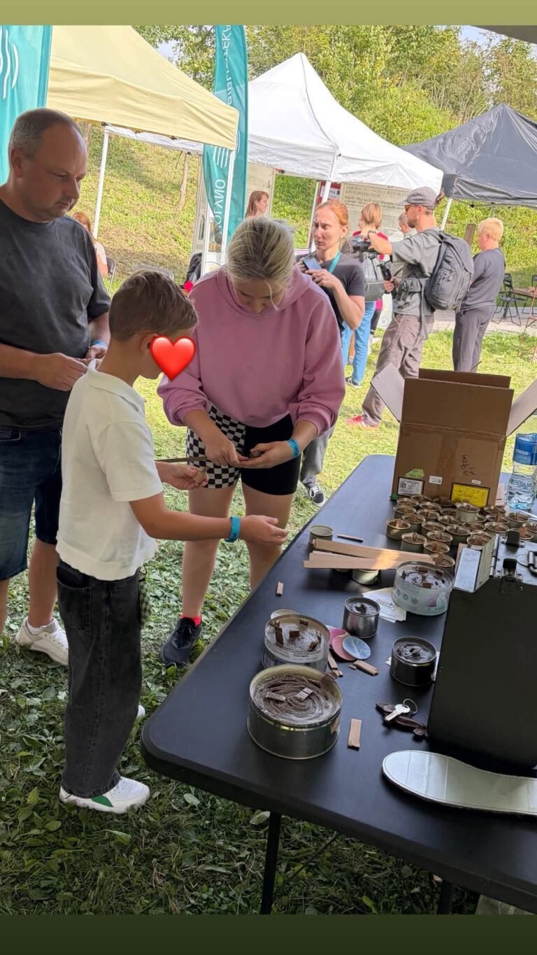 Berniukas su savanorės pagalba lanksto kartoną apkasų žvakės paruoštukui „Visi išvien“ palapinėje IV forte
