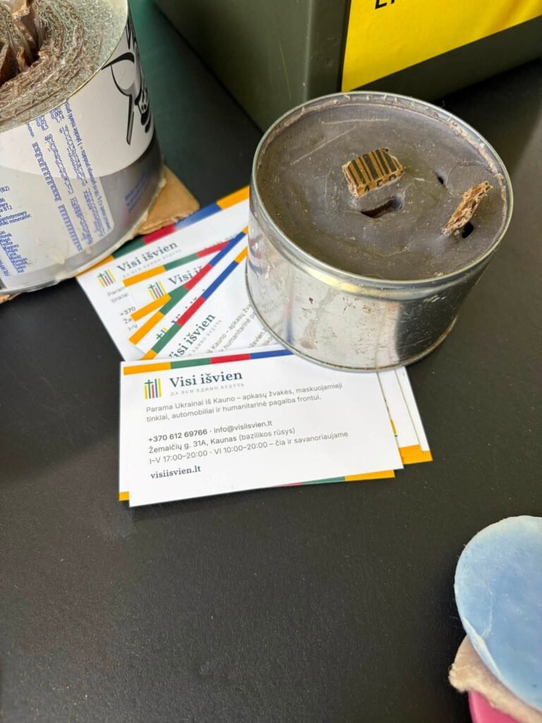 Užpilta apkasų žvakė skardinėje ir fondo „Visi išvien“ vizitinės kortelės ant stalo