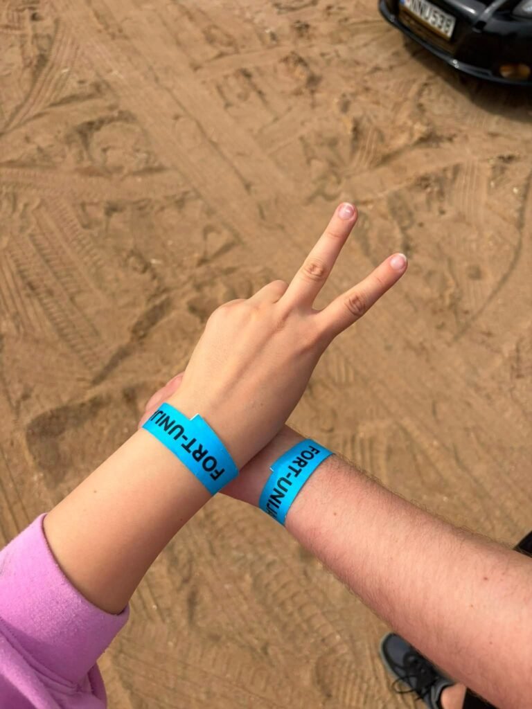 Dvi rankos su mėlynomis festivalio „Fort-Unija“ apyrankėmis, viena rodo pergalės ženklą