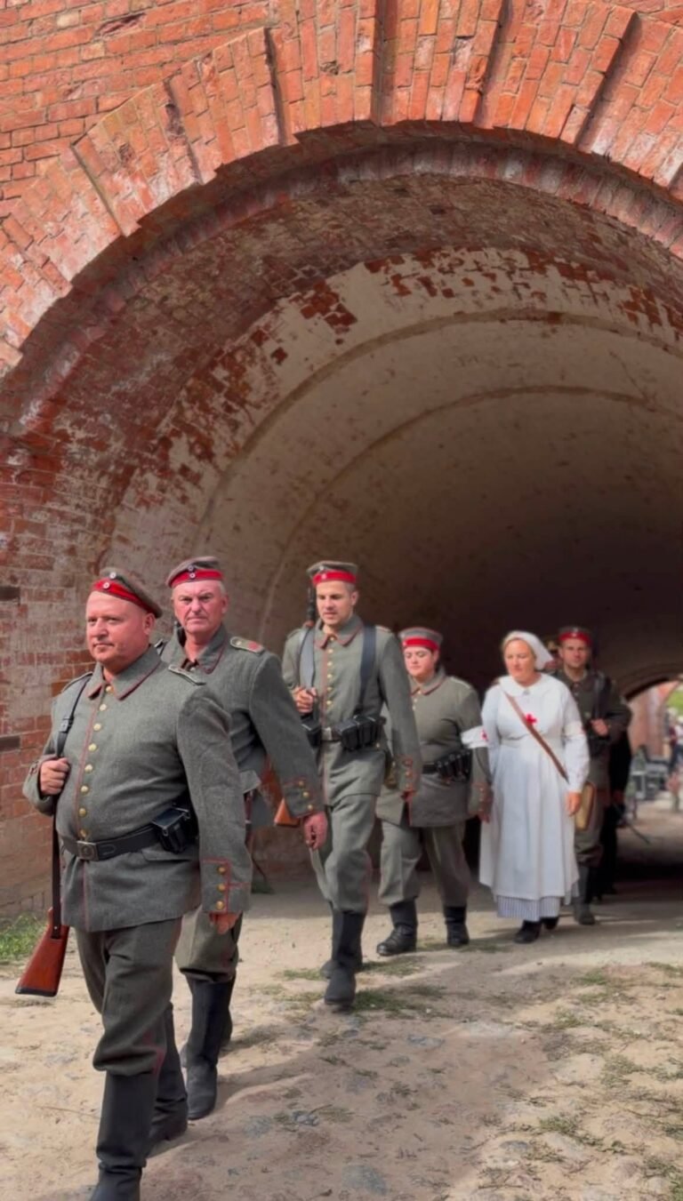 Pirmojo pasaulinio karo uniformomis vilkintys istorinės rekonstrukcijos klubo nariai ir gailestingoji sesuo žygiuoja pro raudonų plytų IV forto tunelį