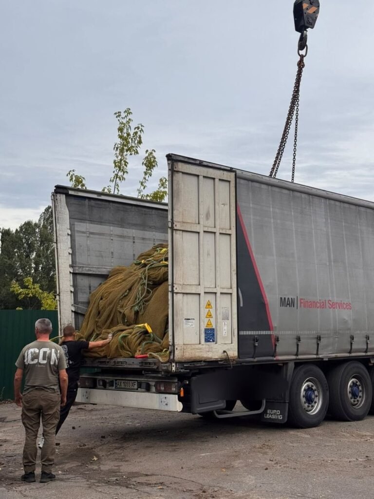 Du vyrai prie puspriekabės, iš kurios kranu iškraunami jūriniai tinklai