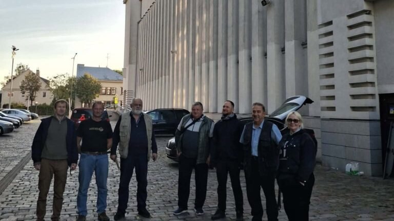 Septyni savanoriai vairuotojai stovi ant grindinio prie Kauno Kristaus Prisikėlimo bazilikos ankstų rytą prieš išvažiuodami į Ukrainą