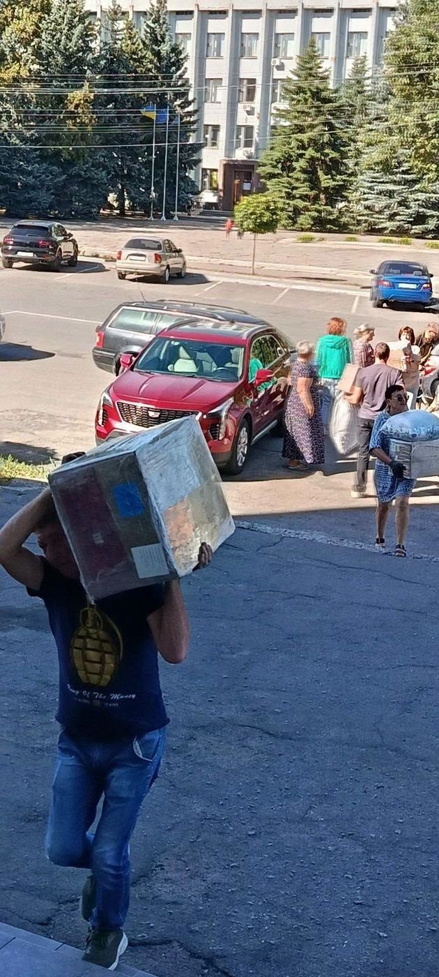 Vyras ant peties neša didelę dėžę su parama nuo automobilių Pyriatyno aikštėje
