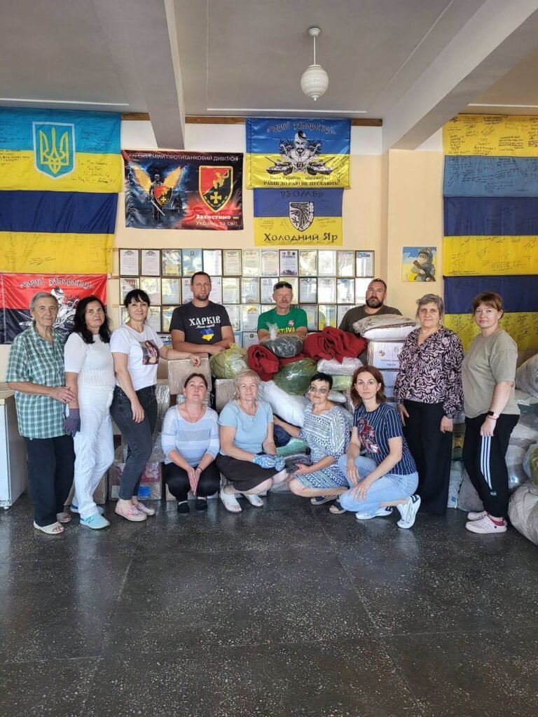 Dvylika žmonių – Pyriatyno savanorių centro savanoriai ir jų svečiai – prie atvežtos paramos, ant sienos Ukrainos vėliavos