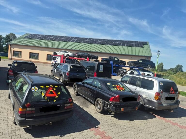 Trys sukabinti automobiliai su avariniais trikampiais ant galinių langų aikštelėje, tolumoje – autovežis