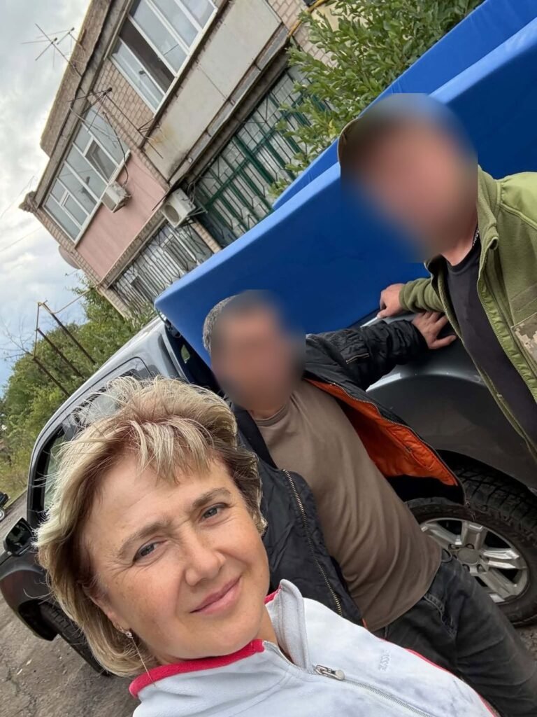 Ukrainos savanorė fotografuojasi su dviem kariais prie pikapo; karių veidai uždengti