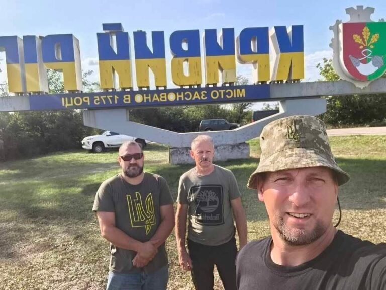 Trys vairuotojai fotografuojasi prie Kryvyj Riho miesto ženklo, nudažyto Ukrainos vėliavos spalvomis